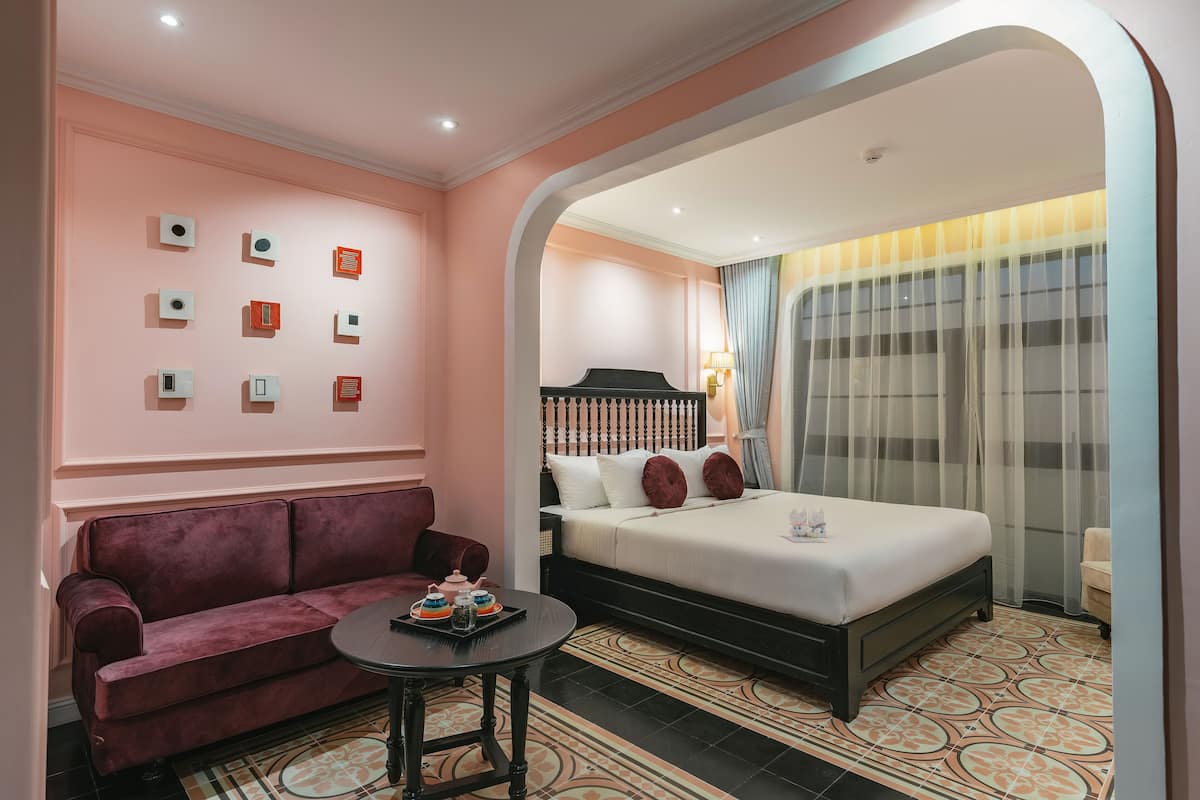 A hotel room with a bed, a sofa, a small table with a tray of items, and a wall with framed pictures.