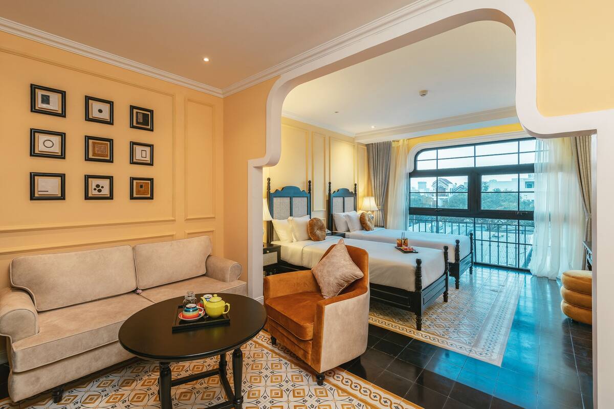 A hotel room with a sofa, armchair, and a bed with a view.