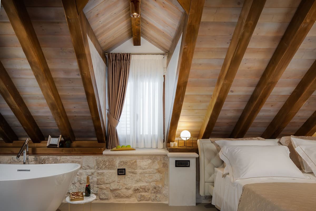 A bedroom with a large bed, a bedside table, a nightstand, and a window with curtains.