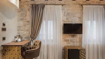 A cozy room with a stone wall, a wooden ceiling, a TV mounted on the wall, a desk with a chair, and a bed.