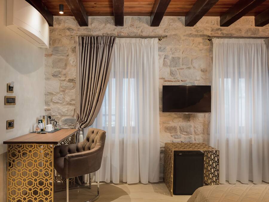 A cozy room with a stone wall, a wooden ceiling, a TV mounted on the wall, a desk with a chair, and a bed.