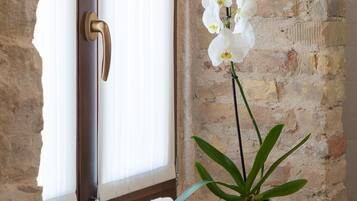 Un baño con pared de piedra, una ventana con puerta de madera y un estante con toallas y una planta en maceta.