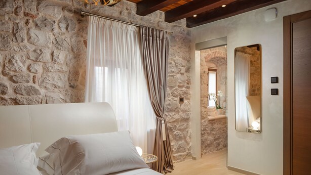 A bedroom with stone walls, a bed with white linens, a large mirror, and a wooden ceiling. - Luxury Rooms MA de Dominis - Adults Only (Split)