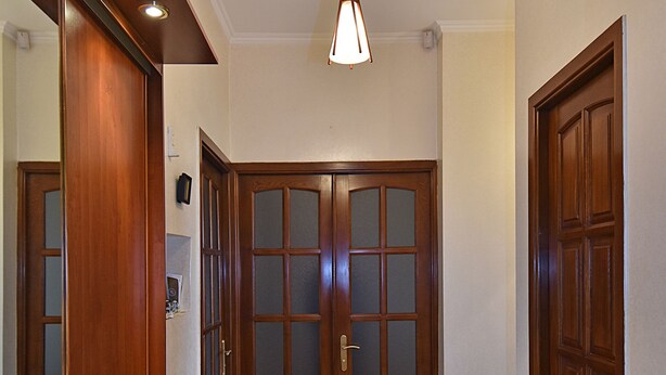 A hallway with wooden doors, a tiled floor, and a hanging light fixture. - Luxury apartment in Yerevan (Arabkir)