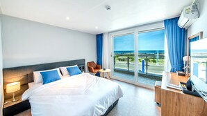 A hotel room with a large bed, a desk, a chair, and a view of the ocean.