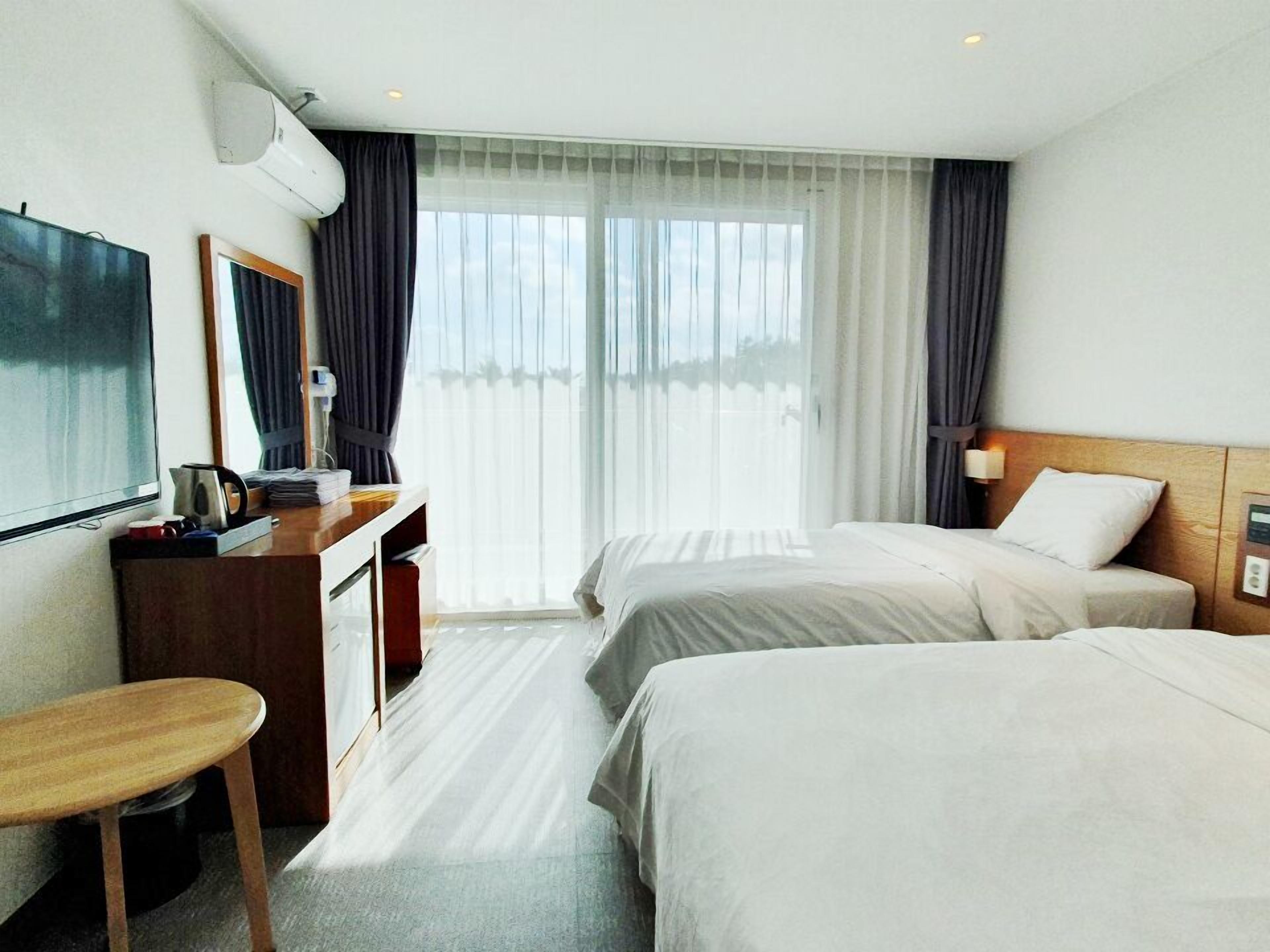 A hotel room with two beds, a desk, a chair, a TV, and a window with curtains.