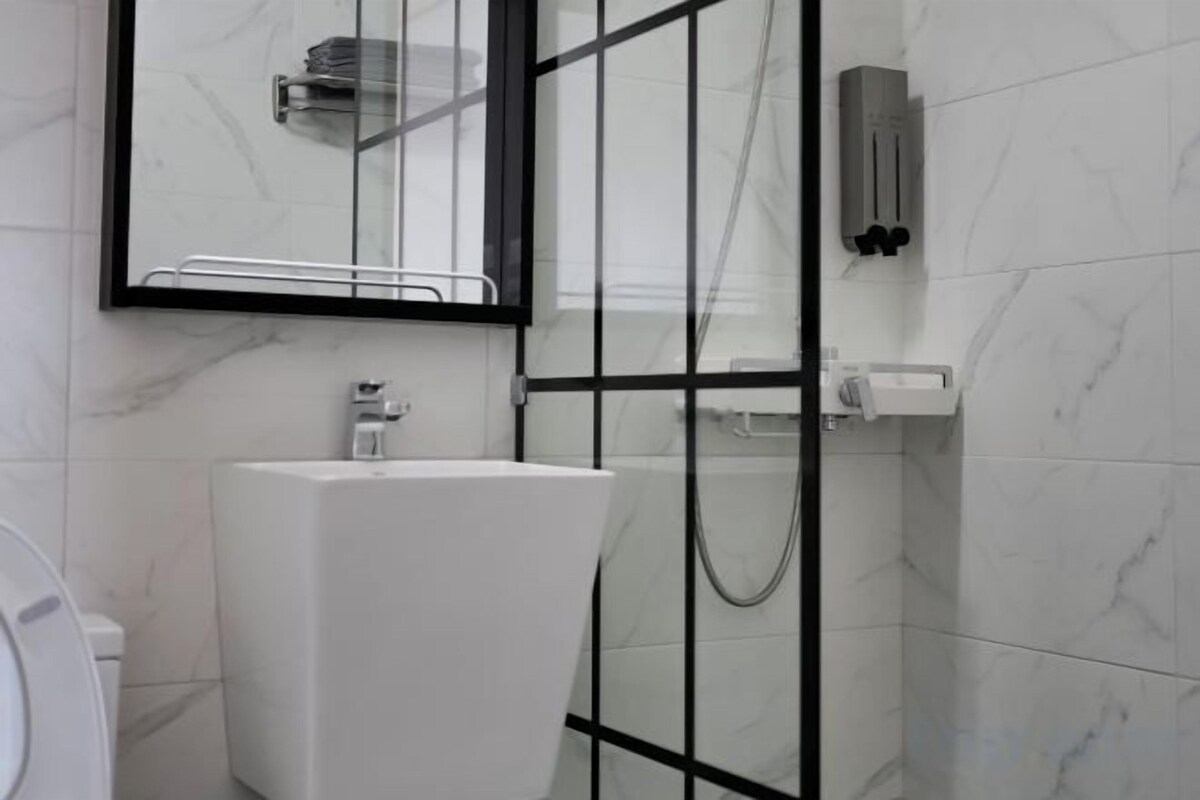 A bathroom with a white sink, a glass shower enclosure, and a mirror with a black frame.