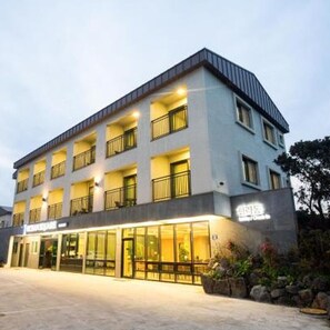 A multi-story hotel with a modern design, featuring balconies on each floor and a ground-level entrance with glass doors. - Jeju Ocean Square Resort (Seogwipo)