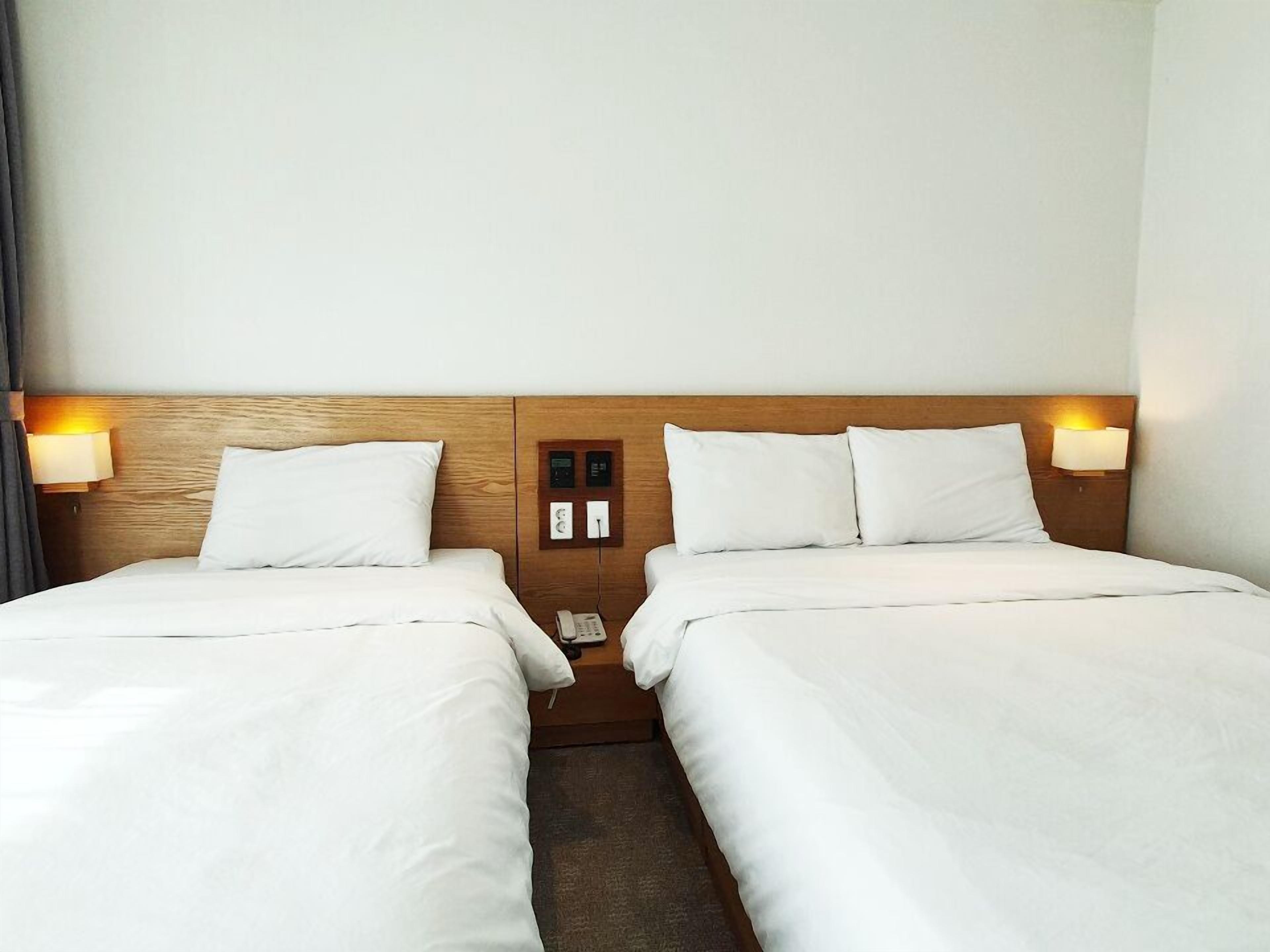 Et hotelværelse med to senge, træhovedgærder, sengeborde med lamper og et kontrolpanel på væggen.