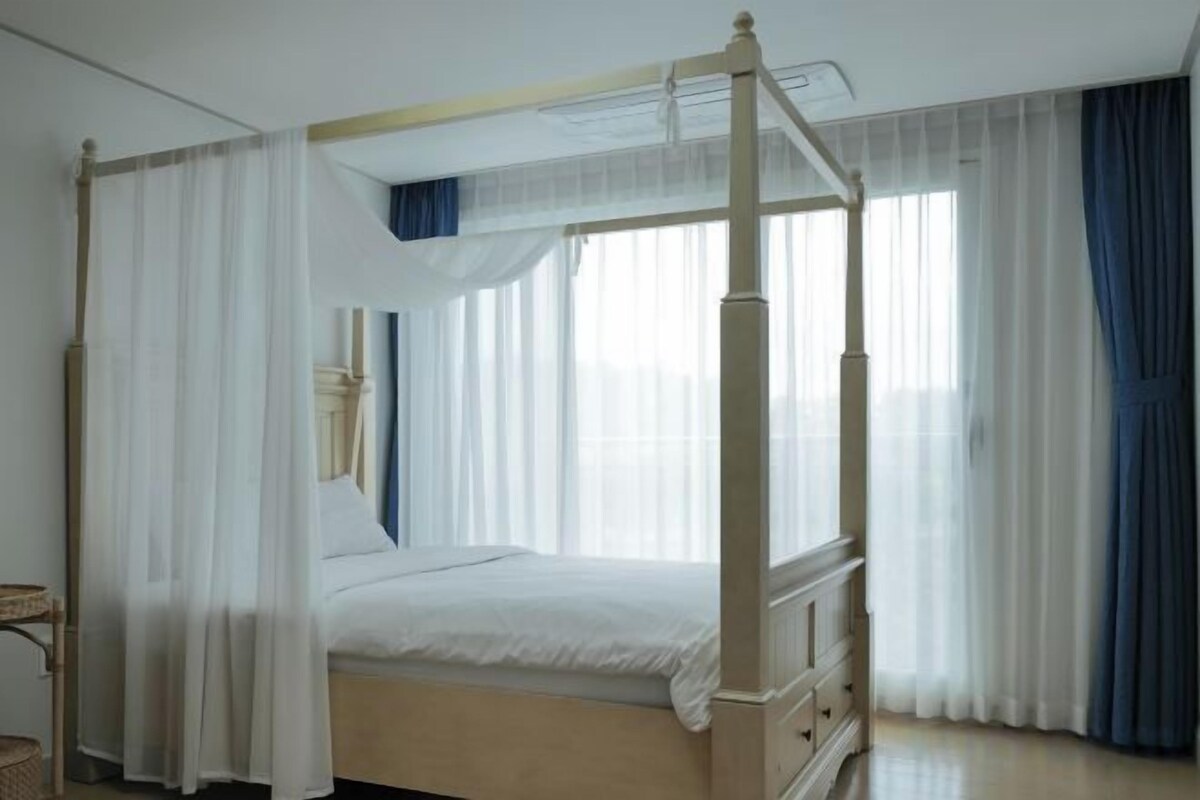 Una cama con dosel y cortinas, una mesita de noche y una ventana con cortinas.