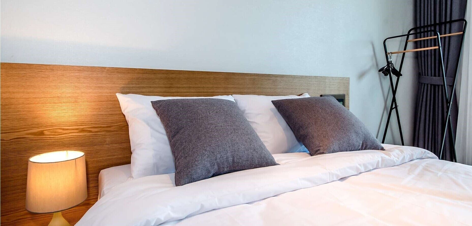 A neatly made bed with white and gray bedding, a wooden headboard, and a bedside lamp.
