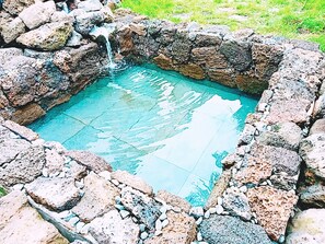 A stone-walled hot spring with clear water, surrounded by rocks. - Jeju Ocean Square Resort (Seogwipo)