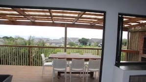 Um deck de madeira com mesa e cadeiras, uma pequena mesa redonda, e vista para casas ao fundo.