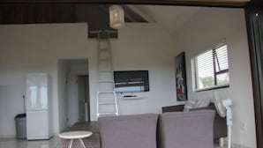 Uma sala de estar moderna com um sofá cinza, uma mesinha branca, uma TV fixada na parede e uma escada.