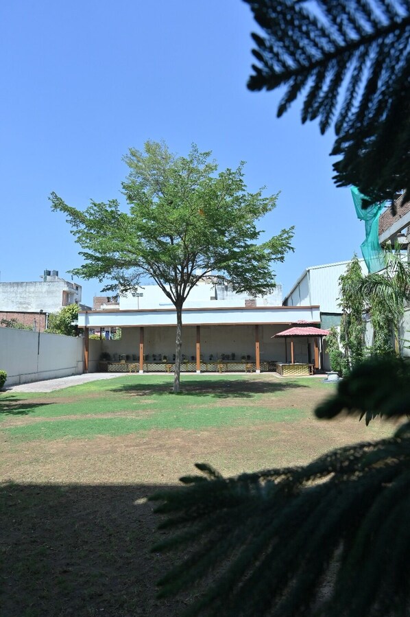 Un edificio con un patio cubierto, un árbol en primer plano y un cielo azul despejado.