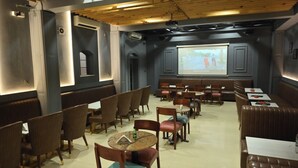 Ein Restaurant mit Sitzecken und Tischen, einer Holzbalkendecke und einer Projektionsleinwand an der Wand.