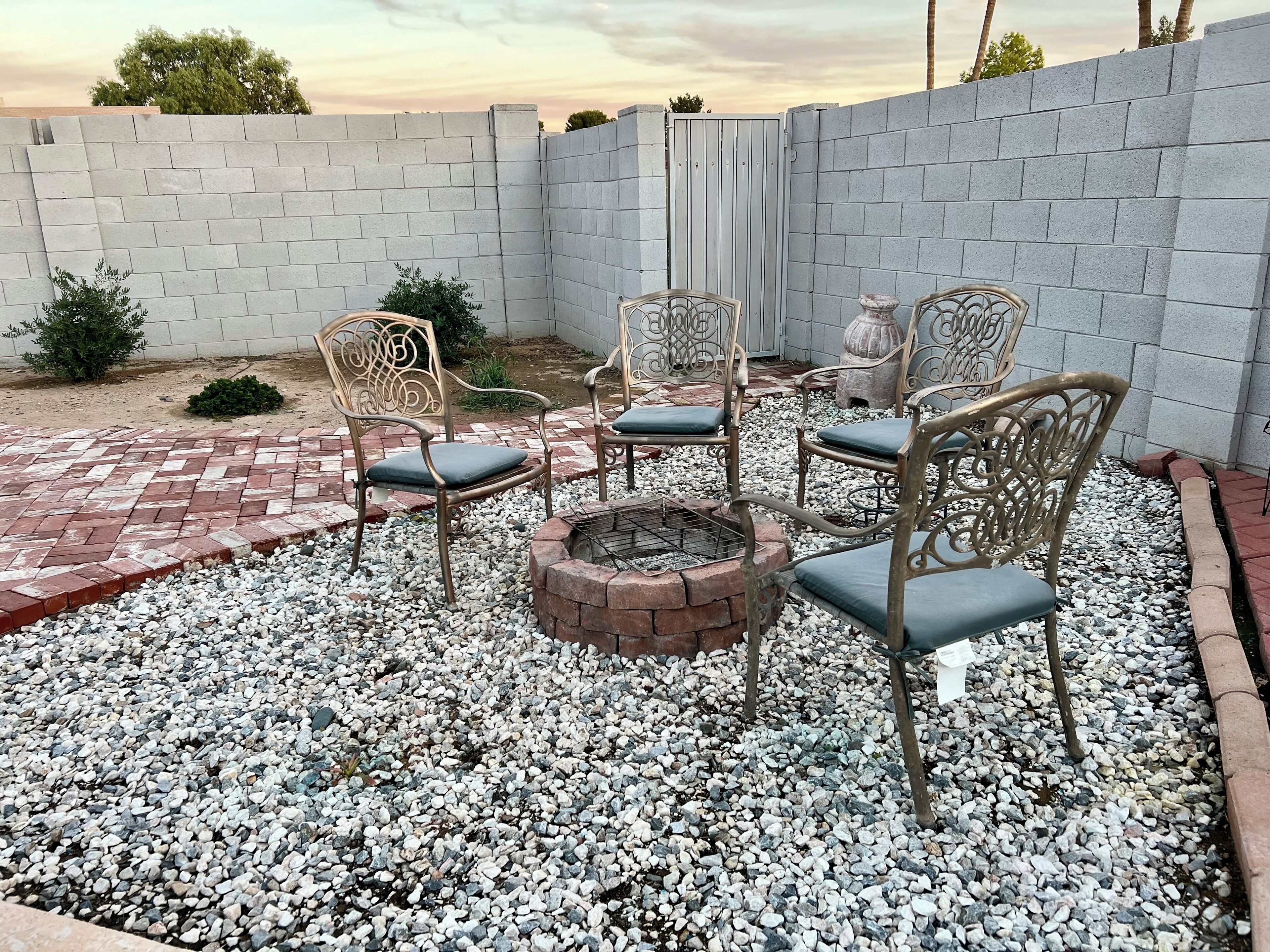 Un espace patio avec un foyer, quatre chaises en métal avec des coussins et un mur en briques.