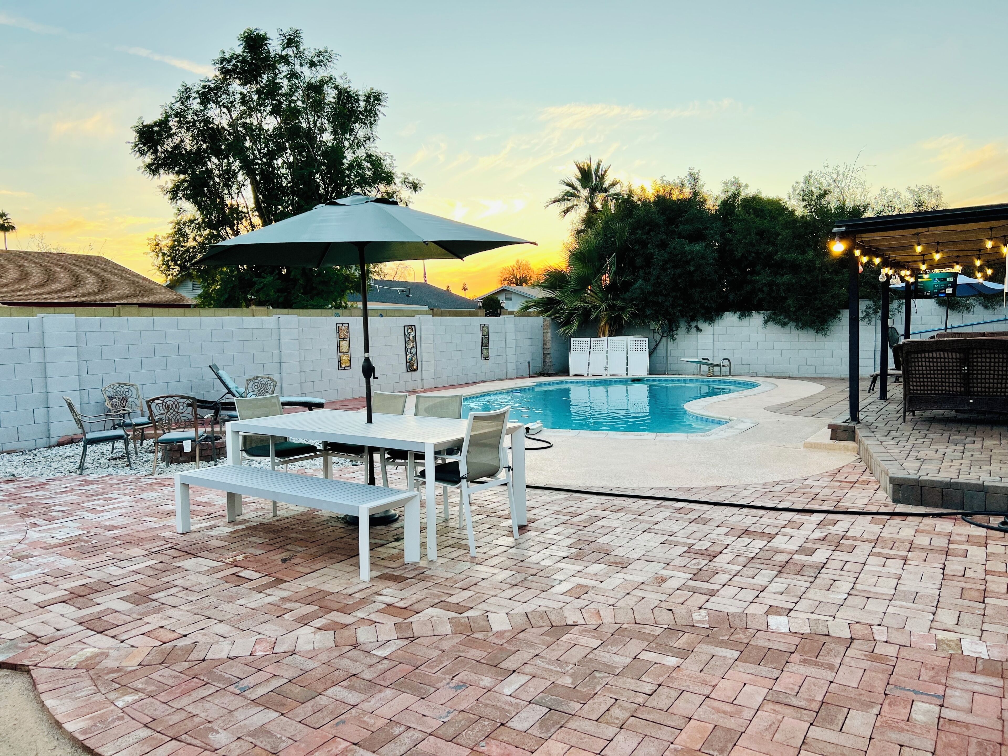 Un patio trasero con piscina, mobiliario de jardín y una zona de estar cubierta.