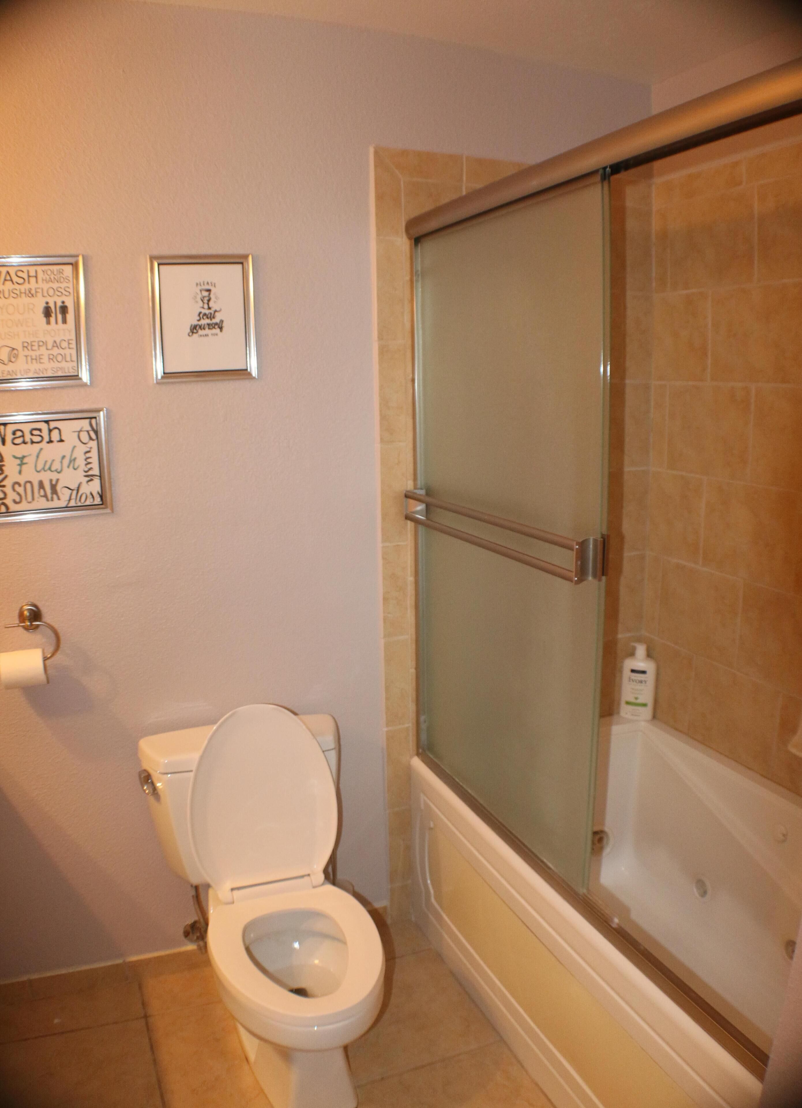 A bathroom with a toilet, a glass shower enclosure, and a bathtub. There are framed signs on the wall with bathroom instructions.