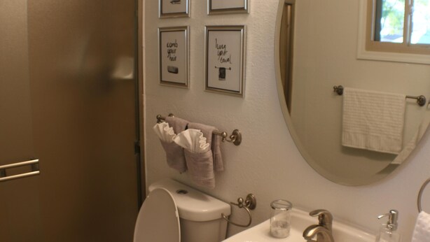 Ein Badezimmer mit Toilette, Waschbecken und Spiegel. An der Wand befinden sich Bilder in Rahmen und ein Handtuch hängt dort.