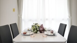 Mesa de comedor preparada para cuatro personas, con un jarrón de flores, vasos transparentes y platos.