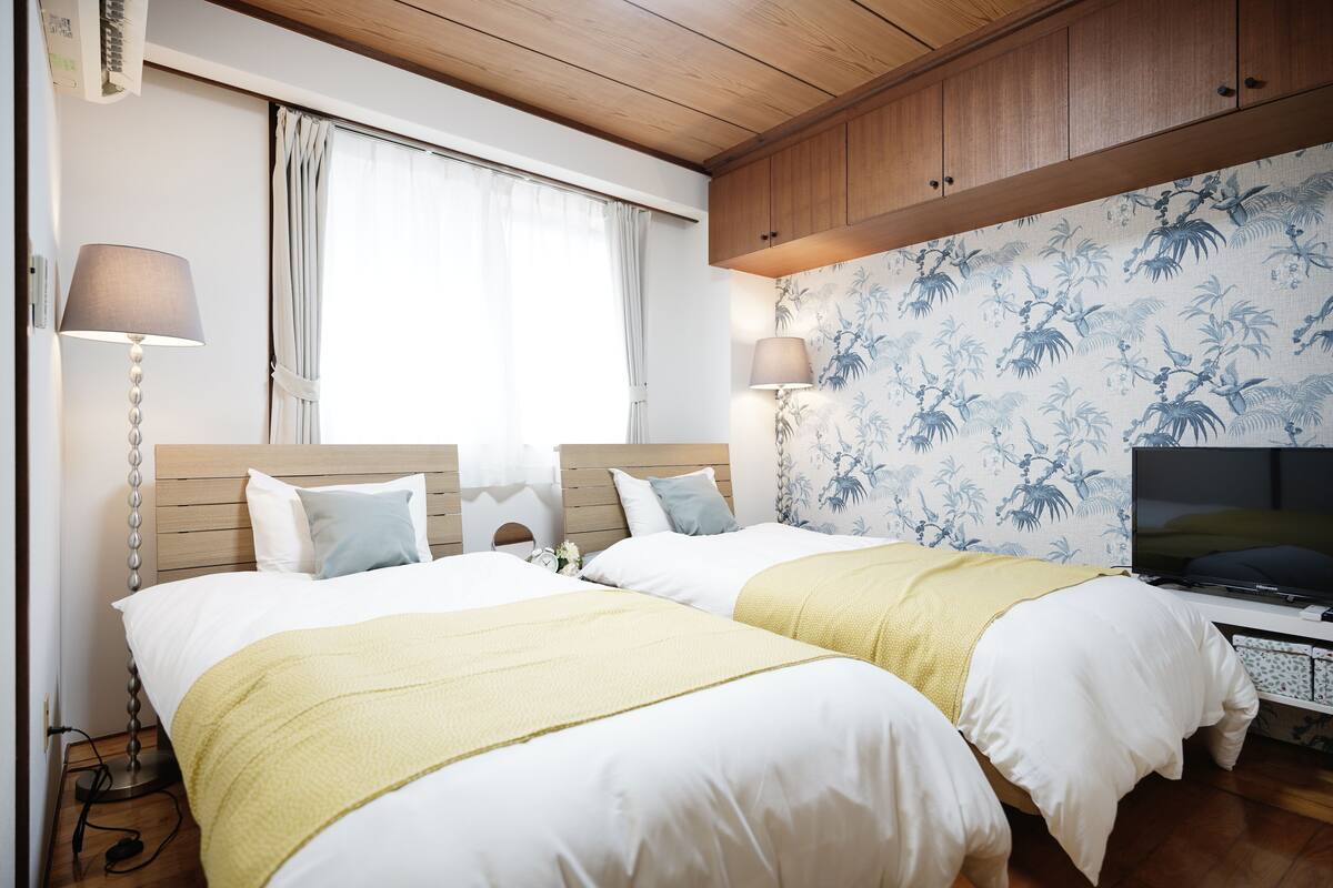 Habitación doble con cama y cabecera de madera, televisor y papel tapiz floral.