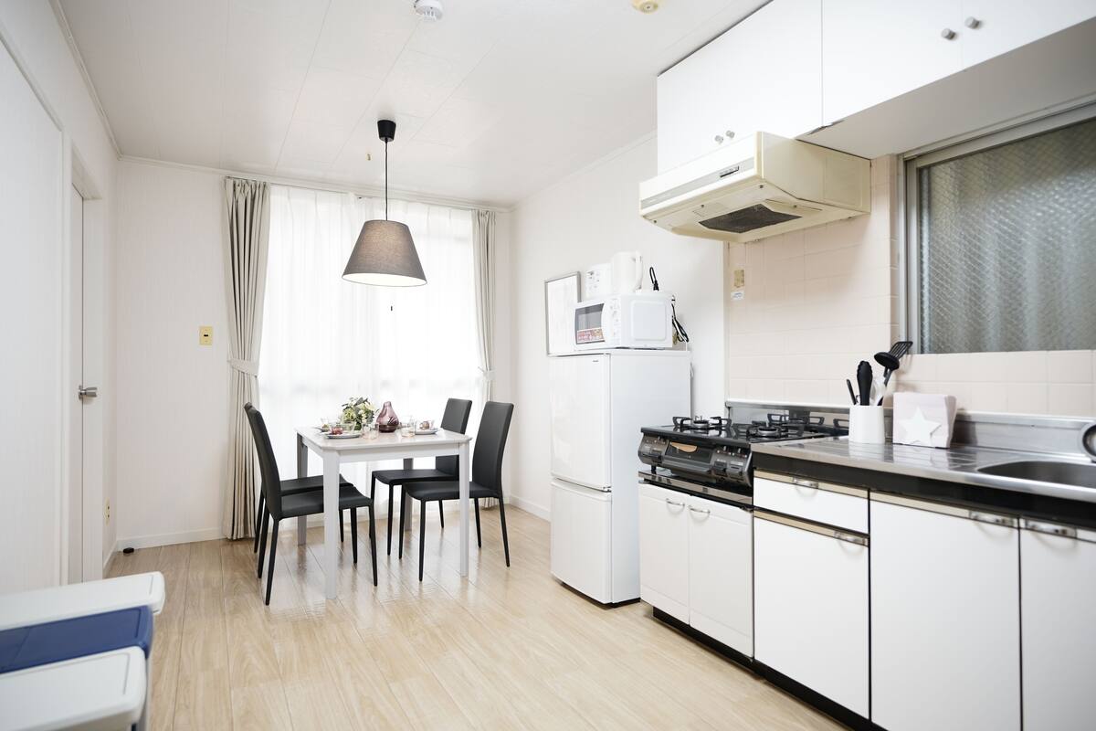 Una cocina moderna con armarios blancos, encimera negra y un comedor con mesa y sillas.