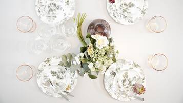 Ein Tisch ist gedeckt mit klarem Glas, tellergroßen Blumenmotiven und einer Mittelanordnung aus Blumen und Grünpflanzen.