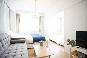 Een moderne, goed verlichte kamer met een bank, een bed, een televisie en een kleine tafel met een plant.