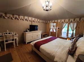 Une chambre à coucher avec un lit, un téléviseur posé sur une commode, un bureau avec une chaise et une fenêtre avec des rideaux.