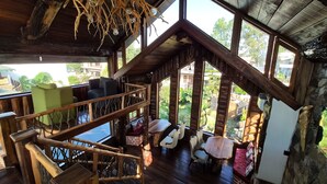 A rustic wooden interior with a staircase, seating area, and large windows offering a view of the surrounding landscape. - Cabana Affair (Dehradun)