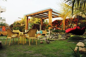 Un jardin agrémenté d’une pergola en bois, de chaises jaunes et d’un fauteuil suspendu.