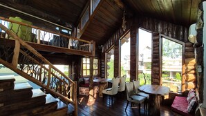 A rustic wooden cabin with a staircase leading to a loft, a dining area with a table and chairs, and large windows offering views of the surrounding landscape. - Cabana Affair (Dehradun)
