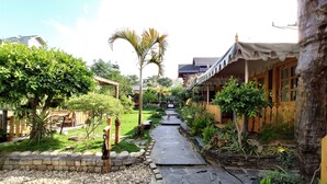 A pathway leading to a wooden house with a covered porch, surrounded by lush greenery and a well-maintained garden. - Cabana Affair (Dehradun)