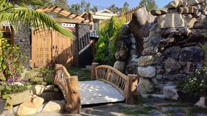 A rustic garden with a wooden bridge, stone walls, and a large wooden gate. - Cabana Affair (Dehradun)