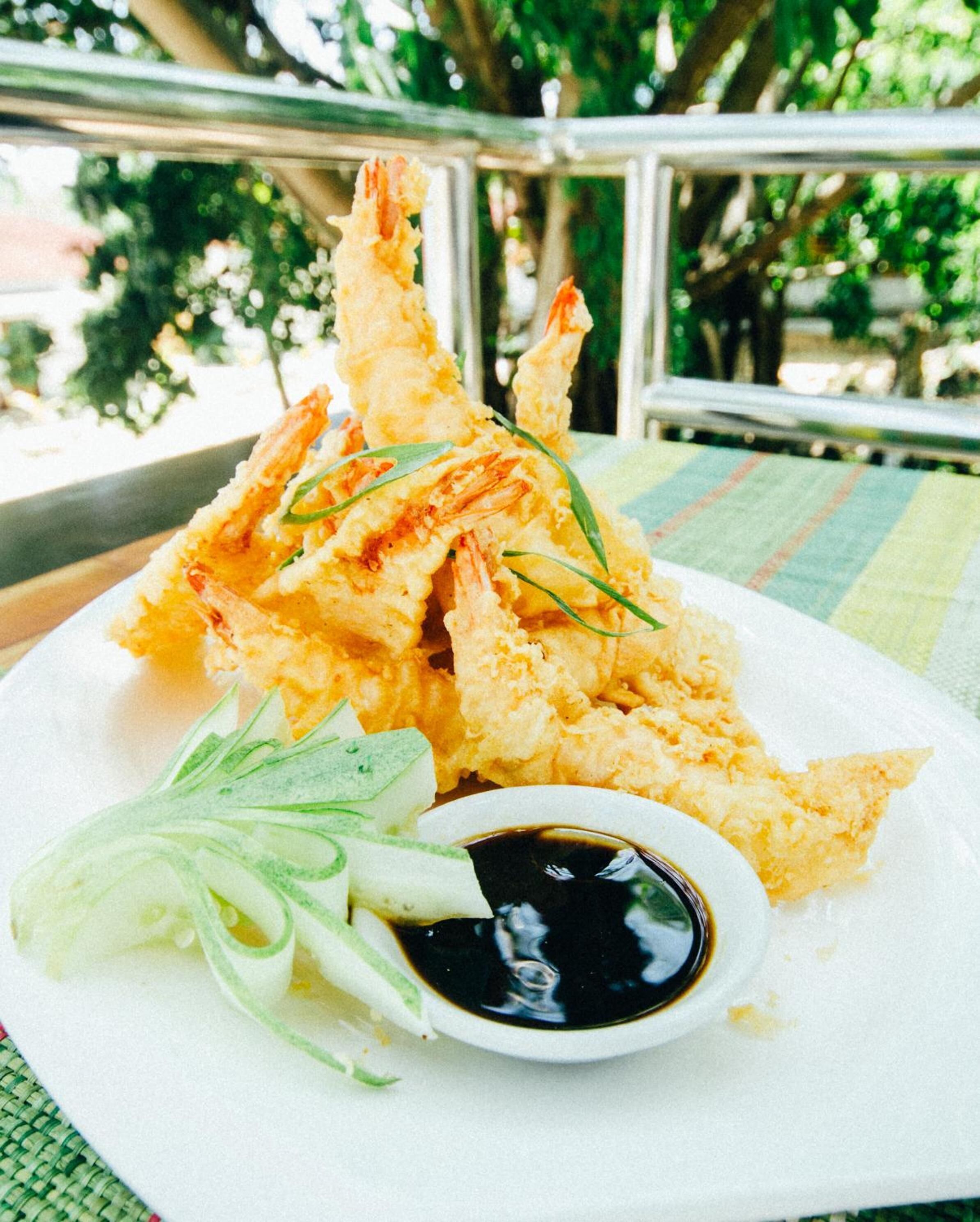 Un plato de camarones tempura con salsa para mojar y jengibre encurtido.