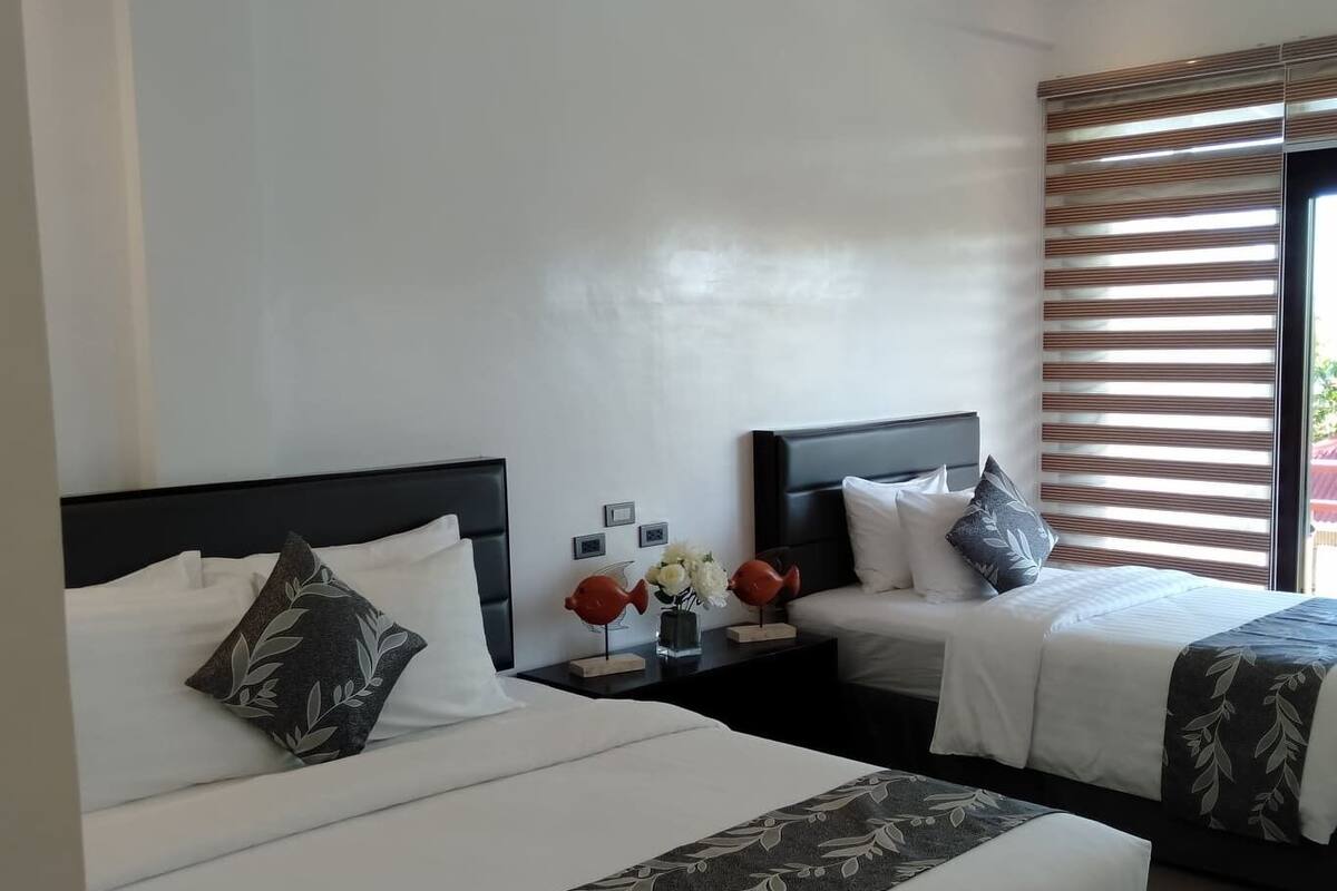 A hotel room with two beds, white bedding, dark headboards, and a window with blinds.