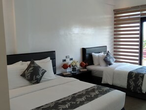 Ein Hotelzimmer mit zwei Betten, weißer Bettwäsche, dunklen Kopfteilen und einem Fenster mit Jalousien.