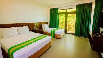 A hotel room with two beds, a wooden headboard, a desk with a television, and a balcony with green curtains.