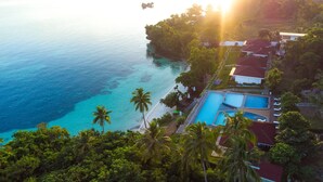 Un resort con piscina, acceso a la playa y abundante vegetación.