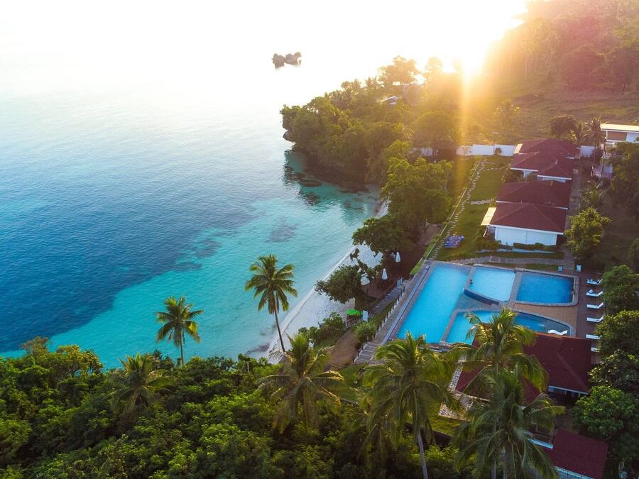 Un resort con piscina, acceso a la playa y abundante vegetación.