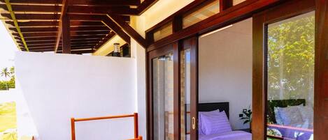 Una habitación con cama, una mesa de madera y un ventanal corredero que da a un balcón.