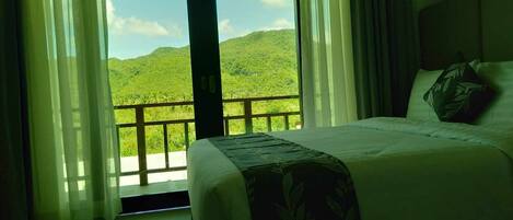 Un dormitorio con cama, vista a un paisaje verde exuberante y un balcón con barandilla.