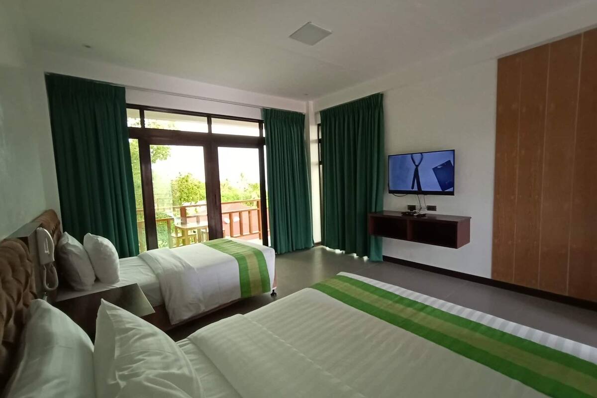 A hotel room with two beds, a TV, and a balcony with a wooden deck.