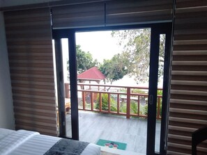Ein Zimmer mit einem Bett, einer Glasschiebetür, die zu einem Außenbereich mit Holzterrasse und einem Gebäude mit rotem Dach führt.