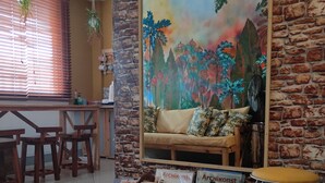 Une pièce chaleureuse avec un mur en pierre, un canapé agrémenté de coussins, une table basse en bois et une fresque représentant des fleurs tropicales.