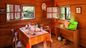 A wooden cabin dining area with a table set for two, chairs, and a window with lace curtains. - Bungalow Village Le Caravelle - by Mamberto S.r.l. (Ceriale)