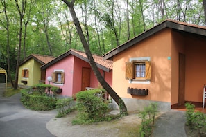 A row of colorful cabins with a dirt path leading to them, surrounded by trees. - Bungalow Village Le Caravelle - by Mamberto S.r.l. (Ceriale)