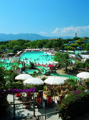 A large outdoor swimming pool surrounded by beach chairs and umbrellas, with a view of mountains in the background. - Bungalow Village Le Caravelle - by Mamberto S.r.l. (Ceriale)