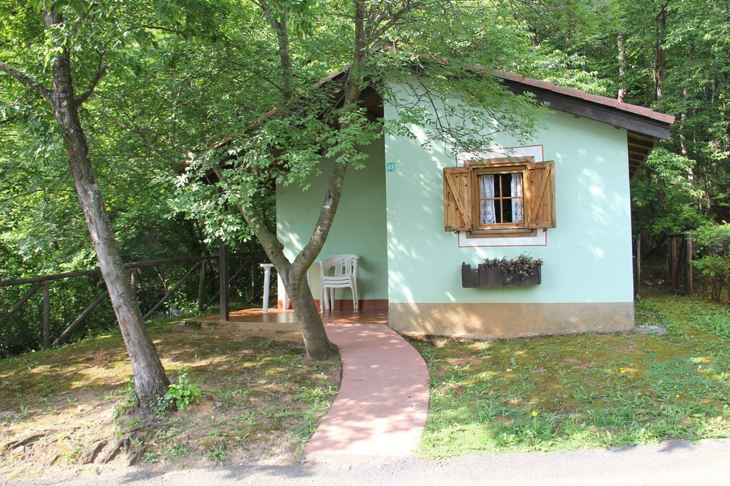 A small, single-story building with a light green exterior, a wooden window with shutters, and a small porch area.